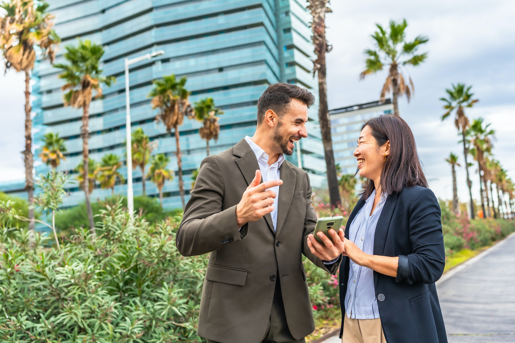 Multi-ethnic male and female business people talking while looking at the smartphones standing in the city