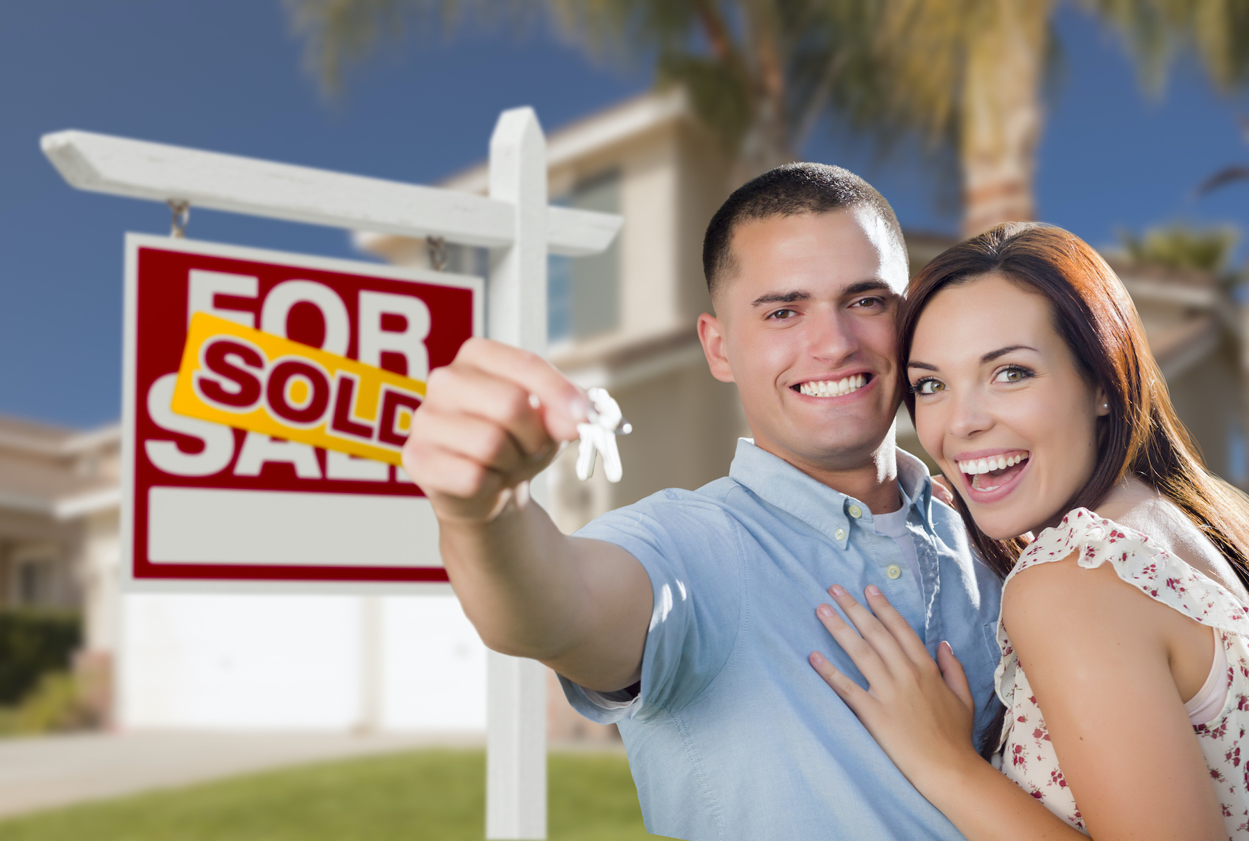 Mixed Race Excited Military Couple In Front of New Home with New House Keys and Sold Real Estate Sign Outside.