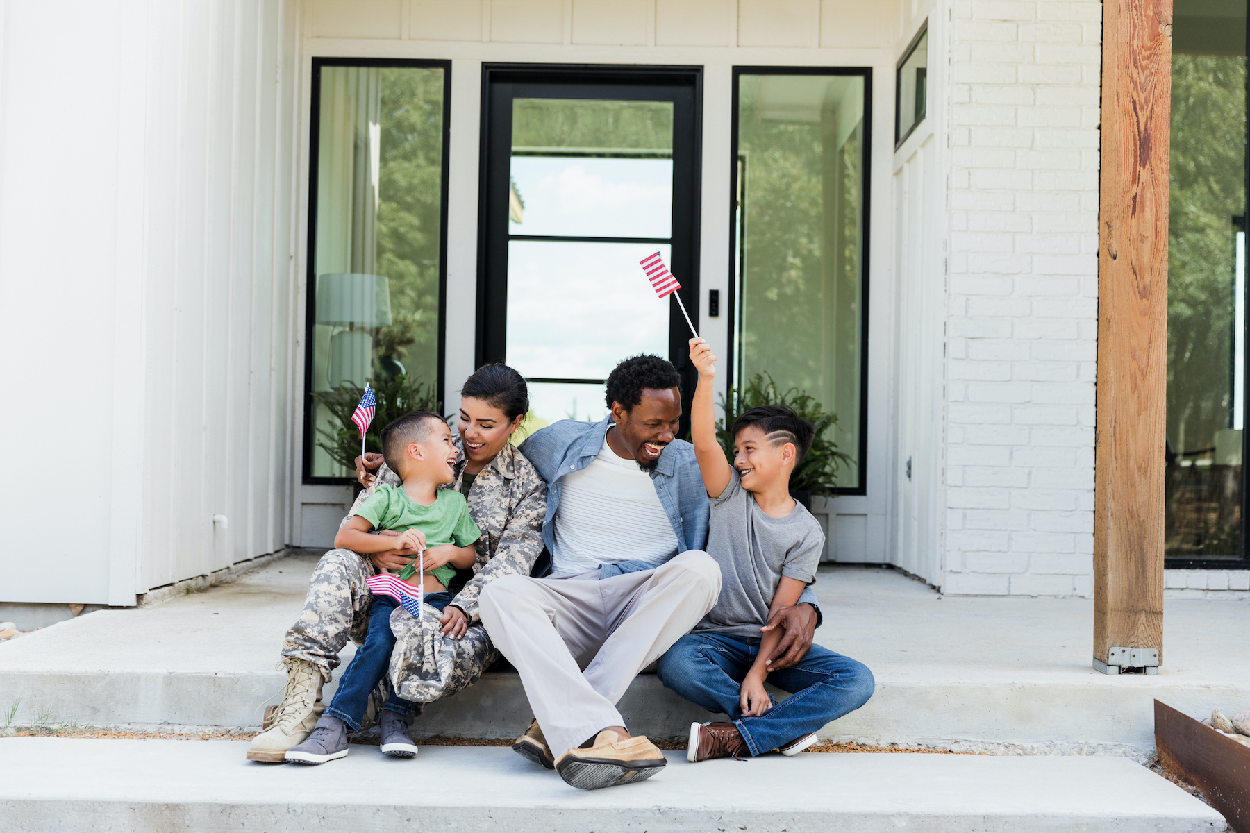Multiracial family with two sons smiles and holds small American flags.