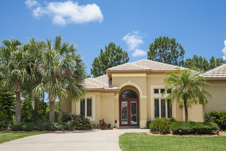 New contemporary home in the tropics with palm trees, tropical foliage, front lawn and driveway. Florida, USA.